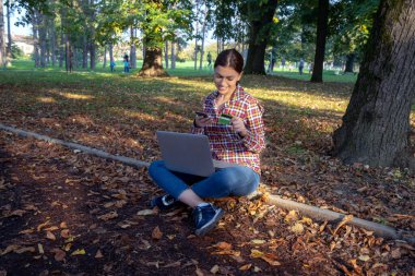 Güzel bir iş kadını, dizüstü bilgisayarlı, telefonla konuşan ve kredi kartı tutan.