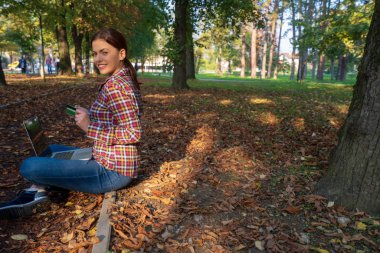 Güzel bir iş kadını, dizüstü bilgisayarlı, telefonla konuşan ve kredi kartı tutan.