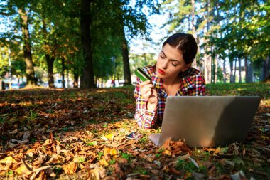Parkta dizüstü bilgisayar ve banka kartı kullanan mutlu kadınlar. İnternetten alışveriş.