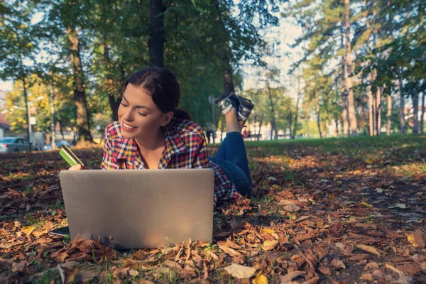 Mujeres felices en el parque usando el ordenador portátil y tarjeta bancaria.Compras en línea — Foto de Stock
