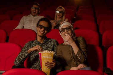 Afrikalı Amerikalı Müslüman adam, karısıyla sinemada oturuyor, 3 boyutlu film izliyor, patlamış mısır yiyor, gülümsüyor..