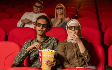 Afrikalı Amerikalı Müslüman adam, karısıyla sinemada oturuyor, 3 boyutlu film izliyor, patlamış mısır yiyor, gülümsüyor..