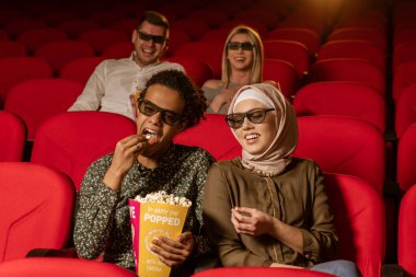 Afrikalı Amerikalı Müslüman adam, karısıyla sinemada oturuyor, 3 boyutlu film izliyor, patlamış mısır yiyor, gülümsüyor..