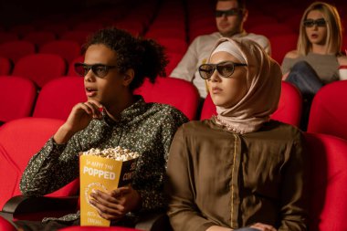 Afrikalı Amerikalı Müslüman adam, karısıyla sinemada oturuyor, 3 boyutlu film izliyor, patlamış mısır yiyor, gülümsüyor..