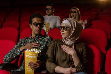 Afrikalı Amerikalı Müslüman adam, karısıyla sinemada oturuyor, 3 boyutlu film izliyor, patlamış mısır yiyor, gülümsüyor..