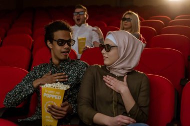 Afrikalı Amerikalı Müslüman adam, karısıyla sinemada oturuyor, 3 boyutlu film izliyor, patlamış mısır yiyor, gülümsüyor..