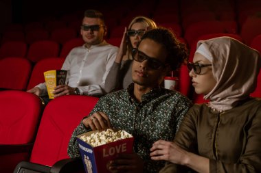 Afrikalı Amerikalı Müslüman adam, karısıyla sinemada oturuyor, 3 boyutlu film izliyor, patlamış mısır yiyor, gülümsüyor..