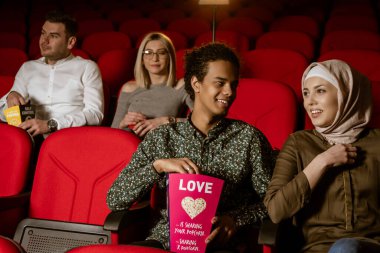 Afrikalı Amerikalı Müslüman adam, karısıyla sinemada oturuyor, film izliyor, patlamış mısır yiyor, gülümsüyor..