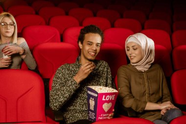 Afrikalı Amerikalı Müslüman adam, karısıyla sinemada oturuyor, film izliyor, patlamış mısır yiyor, gülümsüyor..
