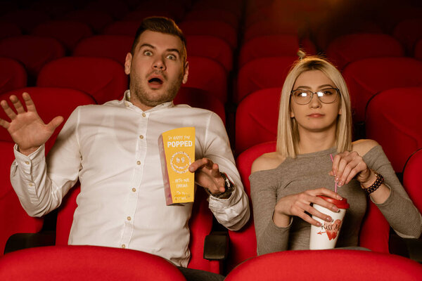 Young loving couple at the cinema watching a movie, eating popcorn, smiling.