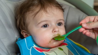 Anne, sevimli bebeğini kaşıkla besliyor.