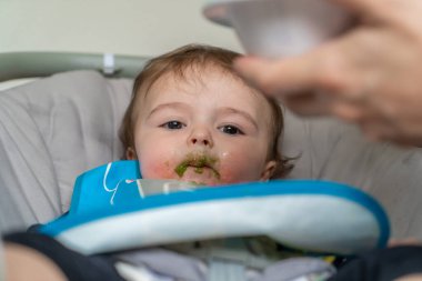 Anne, sevimli bebeğini kaşıkla besliyor.