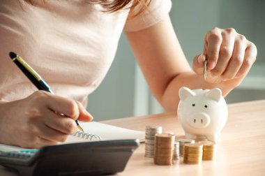 Kumbaraya para koyan bir kadın. Para biriktir ve hesap makinesi kullan