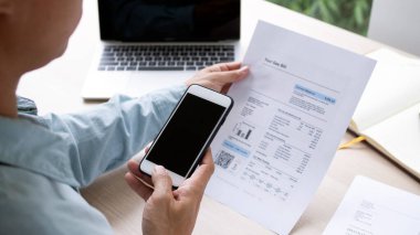 El, QR kodunu taramak için telefonu kullanıyor ve ofiste elektrik faturalarını ödemekten indirim alıyor.