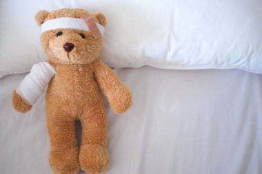 Oyuncak ayı yatakta hasta yatıyordu. Saç bandı ve bezle örtülüydü.