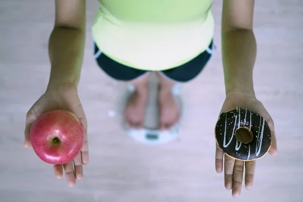 Kobiety Ważą Łuskami Trzymają Jabłka Pączki Decyzja Wyborze Niezdrowej Żywności — Zdjęcie stockowe