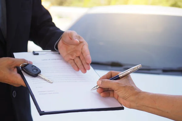 The new car owner signs the lease agreement, contract to receive the key.