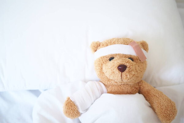 Teddy bear lying sick in bed With a headband and a cloth covered