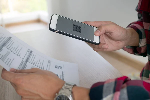 Bir adam eve gönderilen faturayı ödedikten sonra QR kodunu taramak için akıllı telefon kullanıyor. Çevrimiçi fatura ödeme kavramı