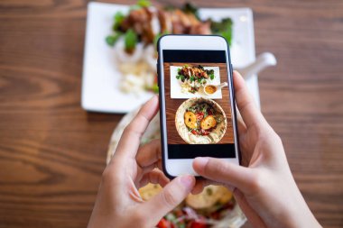Masadaki yemek resimlerini çekmek için cep telefonu kullanan bir kadın. Cep telefonuna yüklendi ve sosyal ağlara yüklendi.