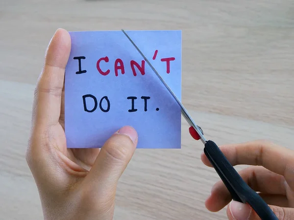 A woman\'s hand is holding a note with the message she wrote when she did not intend. And now she uses the scissors to cut off the letter T because she was inspired by something.