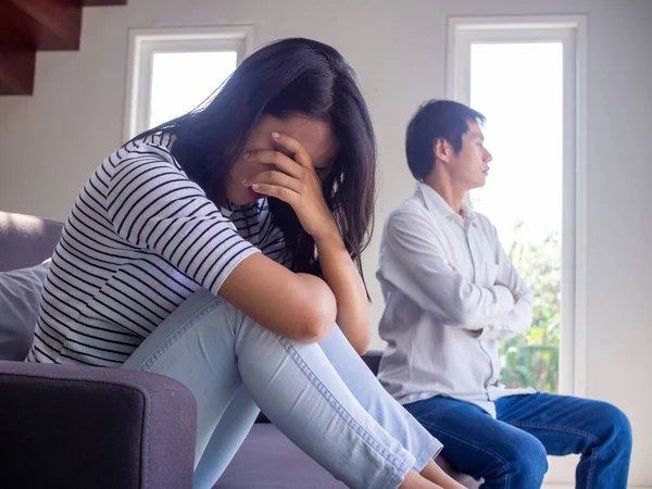 Asian couple have serious quarrel problems sitting on the sofa inside the house. the wife bowed sad. The husband turned his back after a conflict.