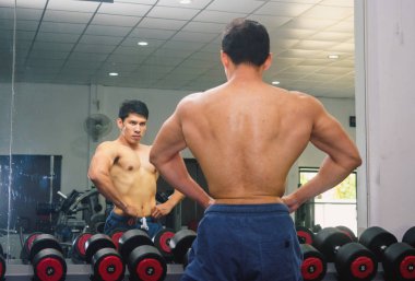 Asyalı genç adam kaslarını bir camın önünde geriyor.