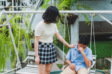 Kız kardeşi üzgün erkek kardeşini bir salıncakta otururken teselli ediyor.