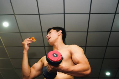 Asyalı adamın kasları var pizza yiyor ve dambılları kaldırıyor.