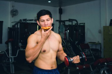 Asyalı adamın kasları var pizza yiyor ve dambılları kaldırıyor.