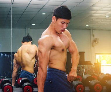 Asyalı genç adam kaslarını bir camın önünde geriyor.