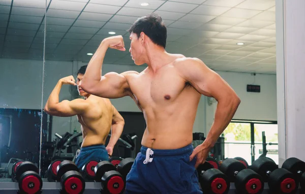 Aziatische jongeman flexing zijn spieren in voor een glas in de g — Stockfoto