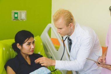 Doktor ve hemşire sethoscop kullanarak kalbi dinliyorlar.