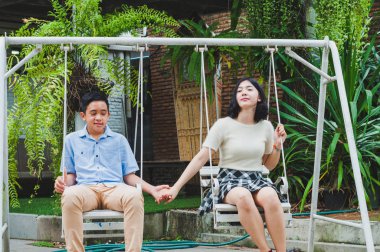 Kız ve erkek kardeş evin bahçesinde salıncak oynuyorlar.