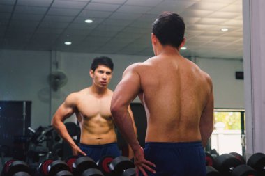 Asyalı genç adam kaslarını bir camın önünde geriyor.