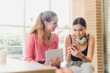 Two beautiful young women playing phone and tablet. concept of r