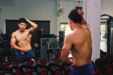 Asyalı genç adam kaslarını bir camın önünde geriyor.