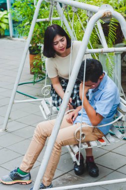 Kız kardeşi üzgün erkek kardeşini bir salıncakta otururken teselli ediyor.