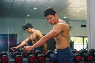 Asyalı genç adam kaslarını bir camın önünde geriyor.