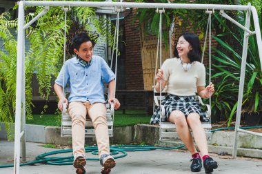 Kız ve erkek kardeş evin bahçesinde salıncak oynuyorlar.