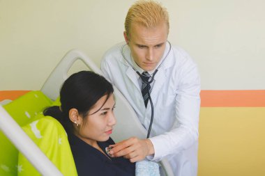 Doktor ve hemşire sethoscop kullanarak kalbi dinliyorlar.