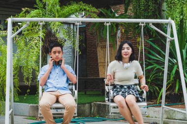 Kız ve erkek kardeş evin bahçesinde salıncak oynuyorlar.