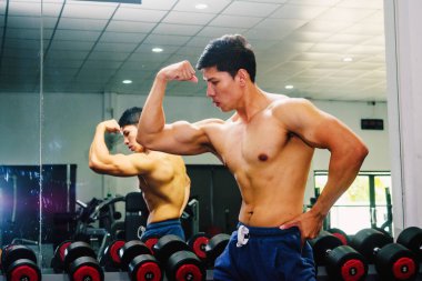 Asyalı genç adam kaslarını bir camın önünde geriyor.