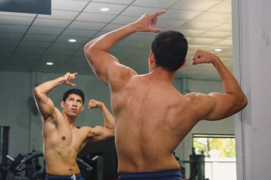 Asyalı genç adam kaslarını bir camın önünde geriyor.