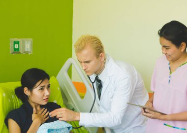 Doktor ve hemşire sethoscop kullanarak kalbi dinliyorlar.