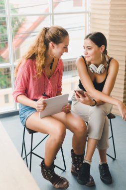 Two beautiful young women playing phone and tablet. concept of r