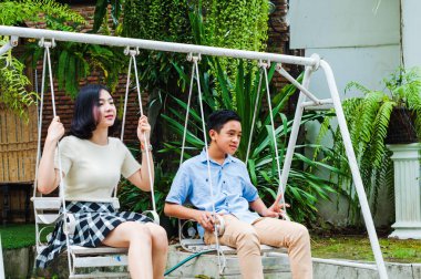 Kız ve erkek kardeş evin bahçesinde salıncak oynuyorlar.