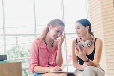 Two beautiful young women playing phone and tablet. concept of r