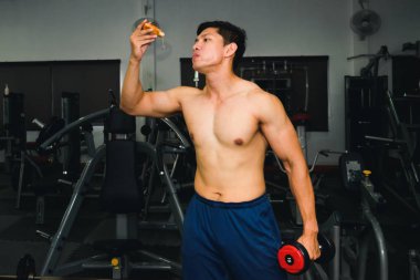 Asyalı adamın kasları var pizza yiyor ve dambılları kaldırıyor.