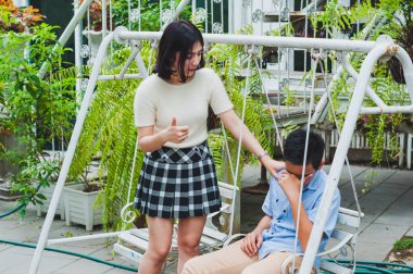 Kız kardeşi üzgün erkek kardeşini bir salıncakta otururken teselli ediyor.